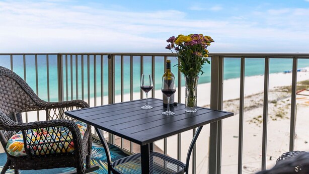 Un balcon avec une table, des chaises, une bouteille de vin et un vase de fleurs.