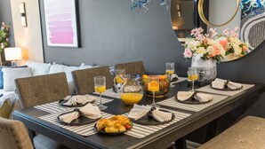 Une table à manger dressée avec des assiettes, des verres et une carafe de jus d’orange, entourée de chaises.