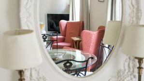 Un salon avec une table ronde en verre, deux fauteuils rouges, un téléviseur et un miroir décoratif.