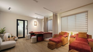 A modern living room with a sofa, ottomans, and a coffee table. There is a sliding door leading to another room.