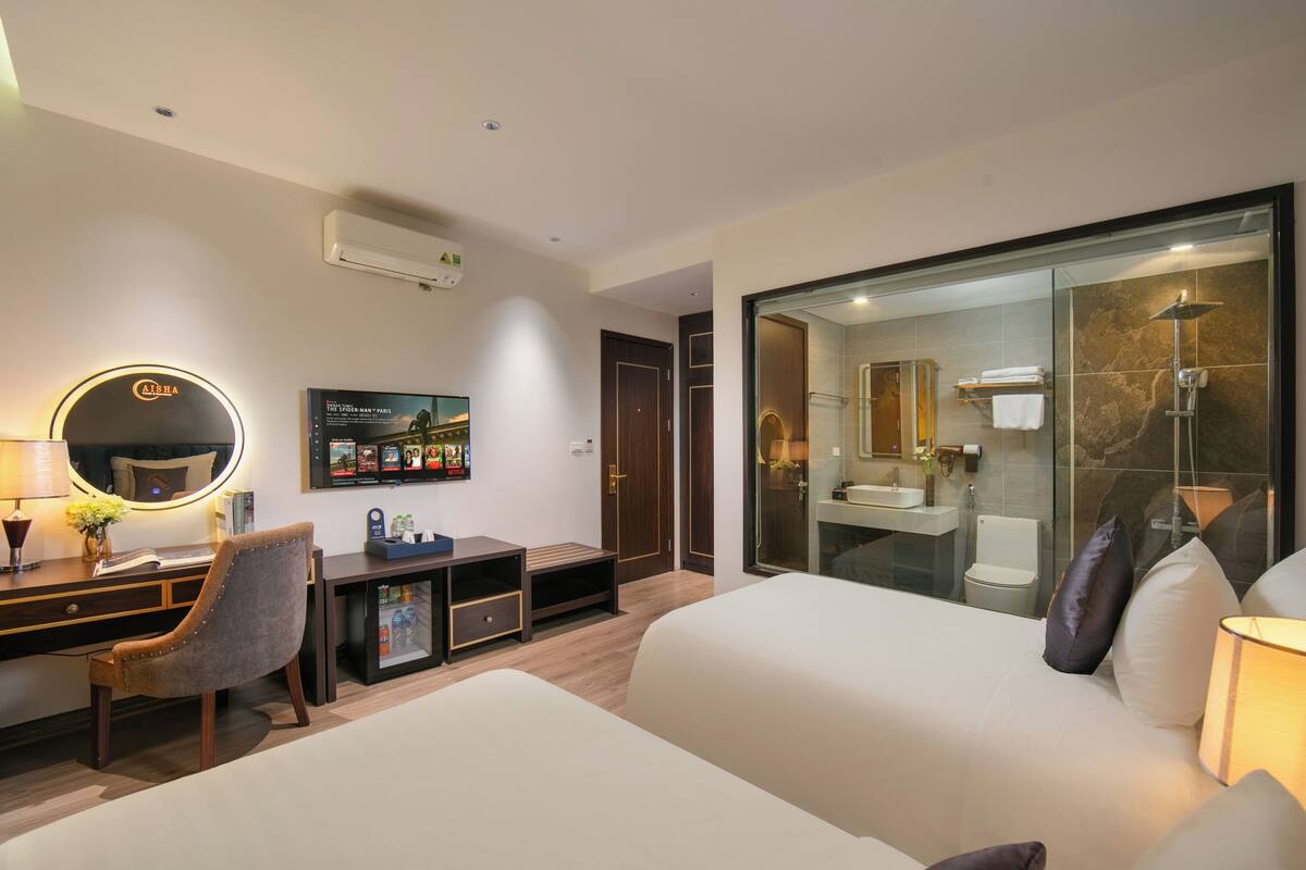 A hotel room with a bed, a desk with a chair, a TV, a mirror, and a bathroom with a shower.
