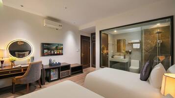 A hotel room with a bed, a desk with a chair, a TV, a mirror, and a bathroom with a shower.
