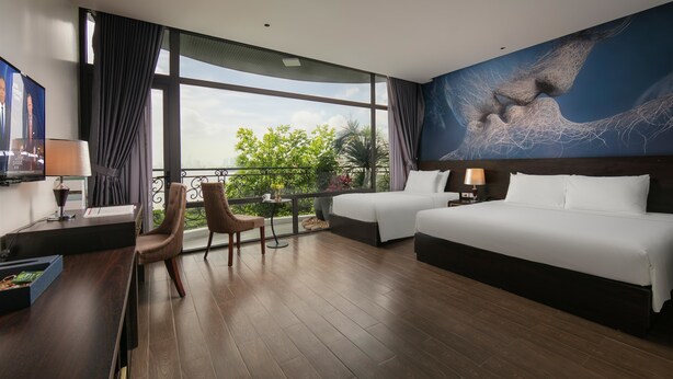 A hotel room with a large window, a bed, a desk with a chair, and a TV.