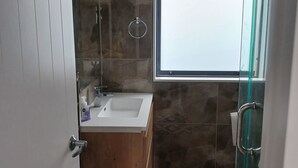 Un baño moderno con tocador de madera, un lavamanos blanco y una cabina de ducha de vidrio.