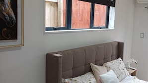Un dormitorio con una cama grande, una mesita de noche, una ventana con contraventanas de madera y un cuadro en la pared.