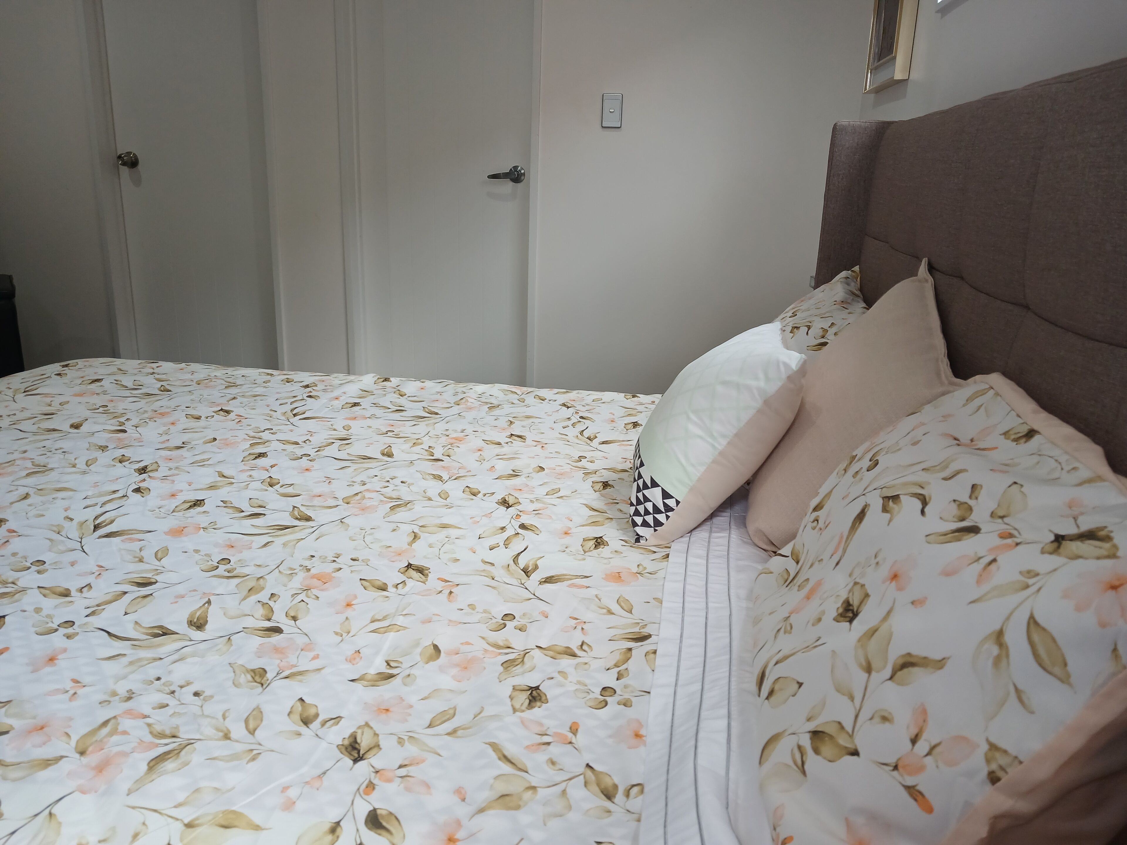 Ein Bett mit blumigem Bettzeug, einem Kopfteil und zwei Kissen.