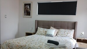 Un dormitorio ordenado con una cama grande, una mesita de noche, una lámpara auxiliar y un televisor de pared, además de un cuadro en la pared.