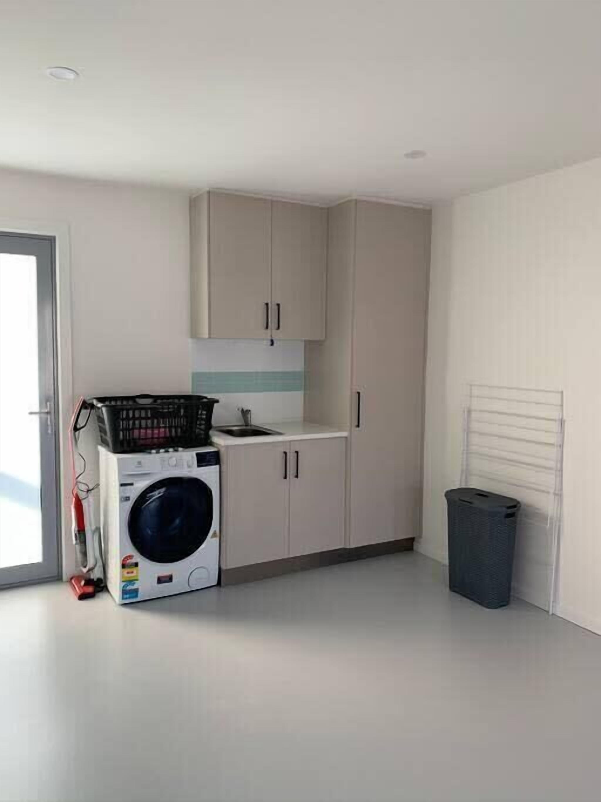 A laundry room with a washing machine, cabinets, and a trash bin.