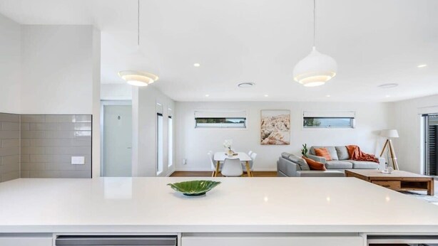 Uma cozinha moderna com uma ilha grande, uma sala de jantar com mesa e cadeiras, e uma sala de estar com sofá e luminária.