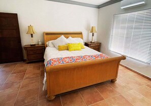 Un dormitorio con una cama de madera, dos mesitas de noche con lámparas, una ventana con persianas y una puerta.
