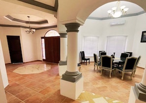 Um quarto amplo com área de refeições, colunas e um lustre.