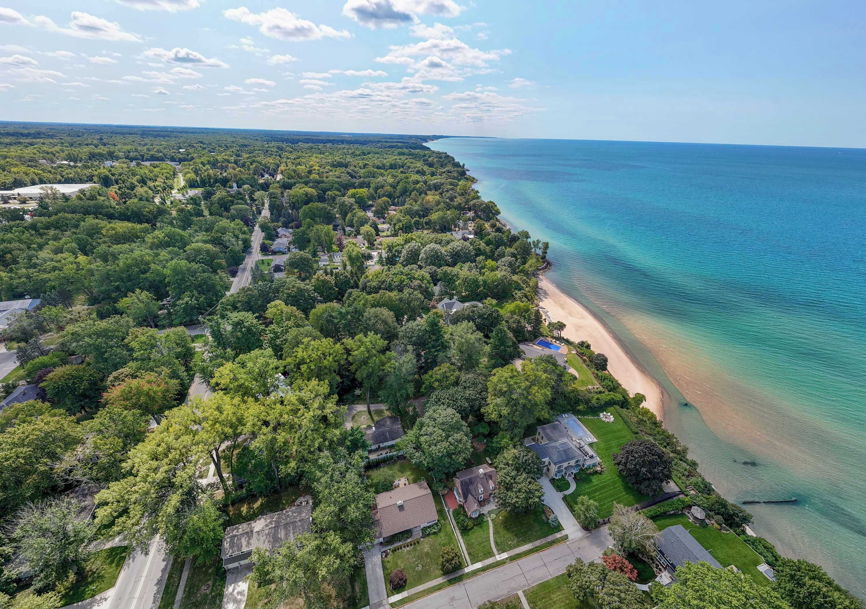 An aerial view of a coastal residential area with houses, a beach, and a clear view of the ocean.