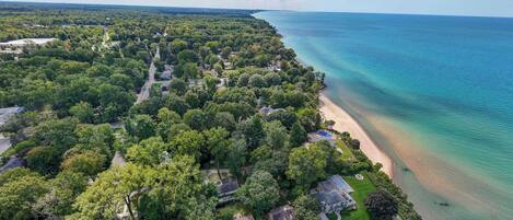 An aerial view of a coastal residential area with houses, a beach, and a clear view of the ocean.