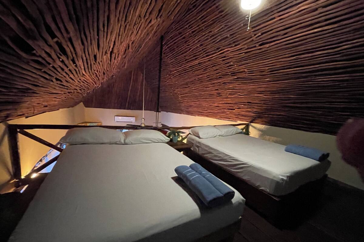 A cozy, tent-like room with two beds, a small table, and a hanging light fixture.