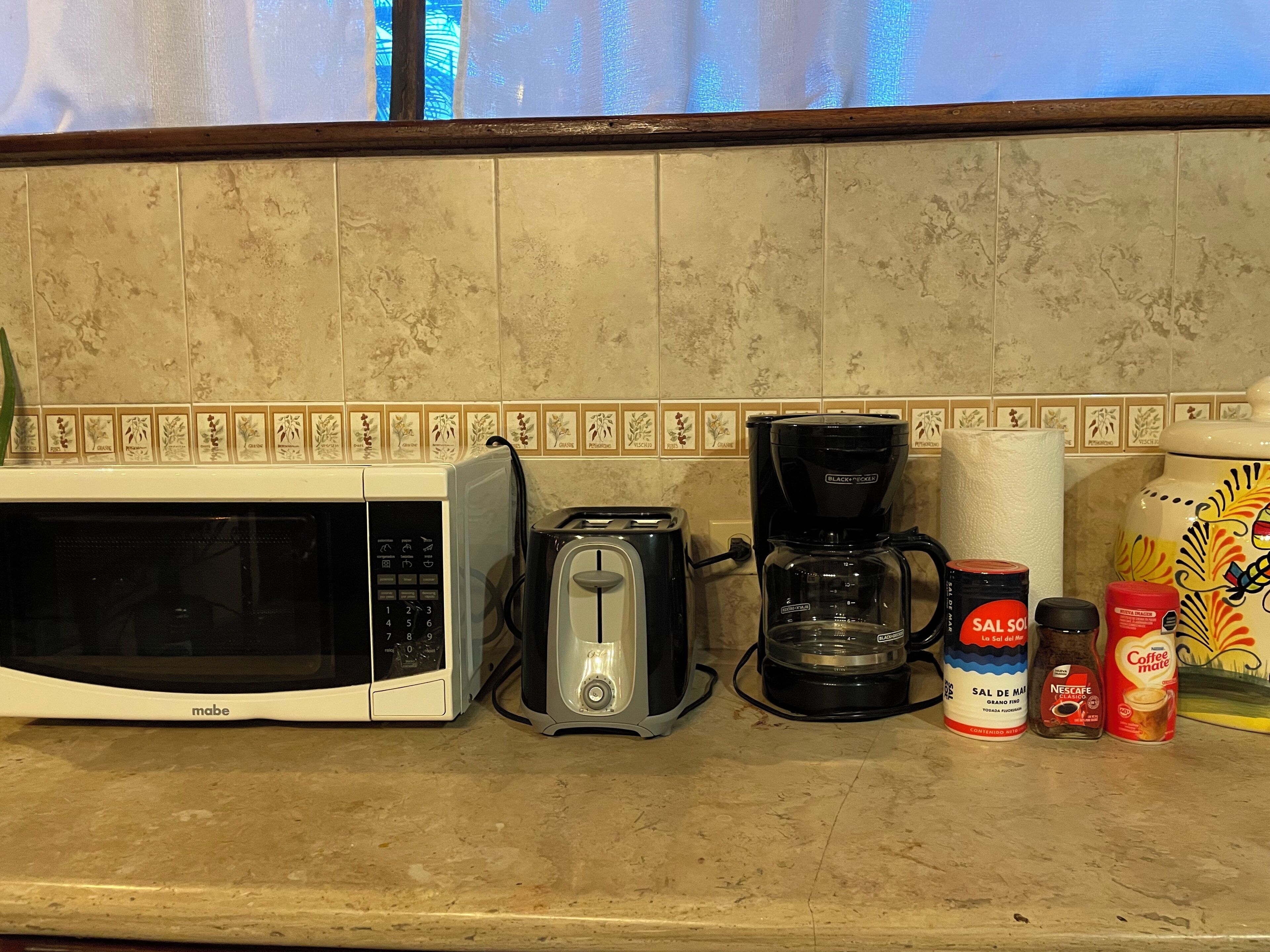 Uma bancada de cozinha com micro-ondas, torradeira, cafeteira e diversos produtos de café.