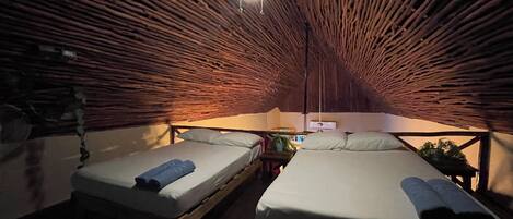 A cozy, rustic room with a sloped ceiling, two beds, a small table, and a ceiling fan.