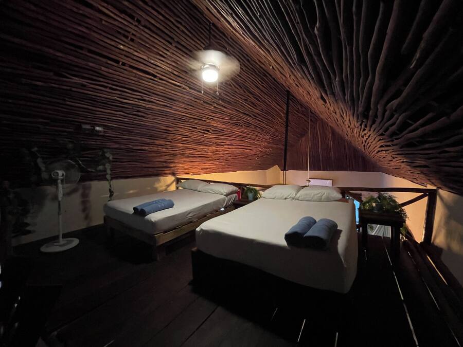 Um quarto aconchegante, com iluminação suave, duas camas, um candeeiro pendente e teto de madeira.