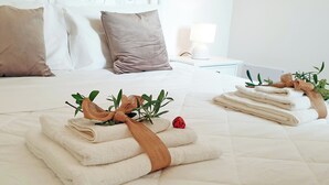A neatly made bed with folded towels and a decorative bow, a bedside table with a lamp, and a window with curtains. - Ladorea Suite - Cozy accommodation with private terrace (San Michele Salentino)