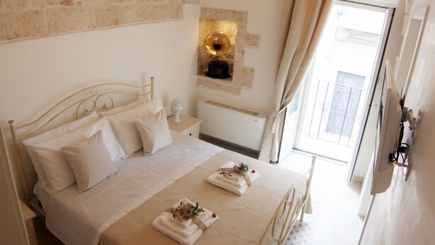 A neatly made bed with white linens and pillows, a bedside table with a lamp, and a view of the outside through a window. - Ladorea Suite - Cozy accommodation with private terrace (San Michele Salentino)