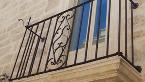 A stone building with a balcony featuring wrought iron railings and a window with a blue-tinted glass. - Ladorea Suite - Cozy accommodation with private terrace (San Michele Salentino)
