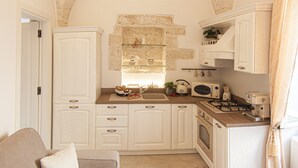 A compact kitchen with white cabinetry, a gas stove, a microwave, and a small dining area with a table and chairs. - Ladorea Suite - Cozy accommodation with private terrace (San Michele Salentino)