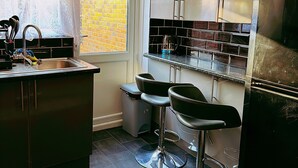 A modern kitchen with a sink, bar stools, and a refrigerator. - Cozy one bed Apartment Near Heathrow (Slough)
