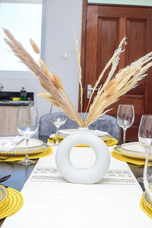 A dining table set with yellow and white plates, clear wine glasses, and a white vase with pampas grass. - 2-bedroom apartment in Mombasa with AC, WiFi (Mombasa)