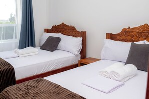Two twin beds with wooden headboards, white linens, and rolled towels. - 2-bedroom apartment in Mombasa with AC, WiFi (Mombasa)