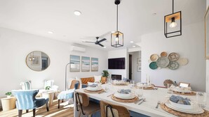 A modern dining area with a long table, chairs, and a ceiling fan. - Walk to the Beach & Pier! | Ocean View Roof Deck (Oceanside)