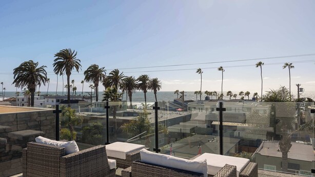 A balcony with wicker furniture, a clear view of the ocean, and palm trees. - Walk to the Beach & Pier! | Ocean View Roof Deck (Oceanside)