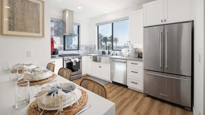 A modern kitchen with white cabinets, stainless steel appliances, and a large window. - Walk to the Beach & Pier! | Ocean View Roof Deck (Oceanside)