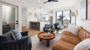 A modern living room with a sofa, armchairs, a coffee table, and a ceiling fan. - Walk to the Beach & Pier! | Ocean View Roof Deck (Oceanside)