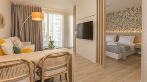 Una habitación de hotel moderna con zona de comedor, sofá, televisor y cama.