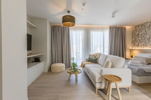 A modern living room with a sofa, a coffee table, and a television on a stand. - The Mediterranean Suites (Piraeus)