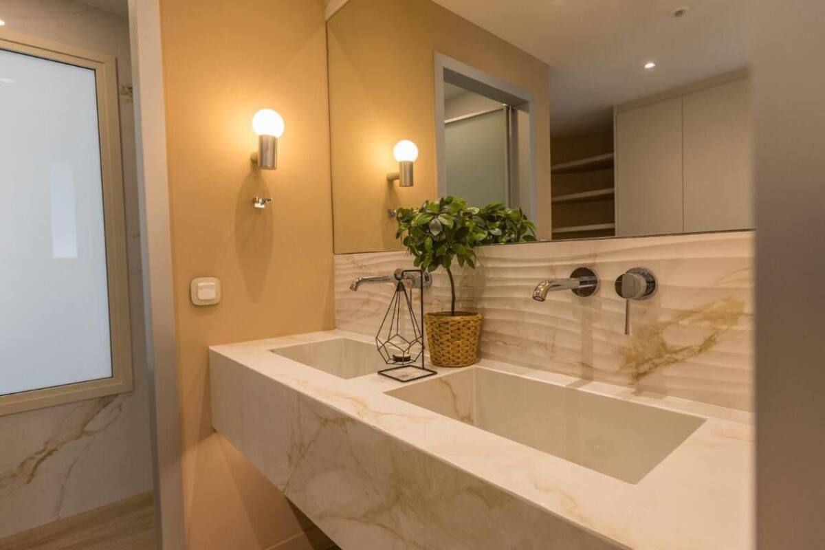 Un baño moderno con un lavamanos grande de mármol, dos luces empotradas, un espejo y una planta en maceta.