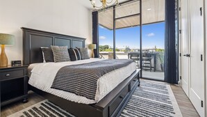 A modern bedroom with a large bed, a chandelier, a nightstand, and a view through a sliding glass door to an outdoor patio. - Music Row, Pool, Rooftop Deck, Balcony, Gym (Nashville)