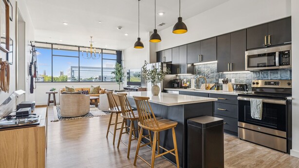A modern kitchen with dark cabinets, stainless steel appliances, and a large island with bar stools. - Music Row, Pool, Rooftop Deck, Balcony, Gym (Nashville)