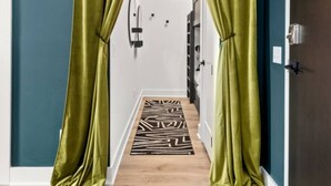 Un pasillo con cortinas verdes, suelo de madera y un rug con estampado de cebra.