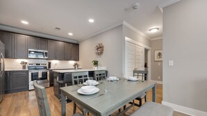 A modern kitchen with dark cabinets, stainless steel appliances, and a dining area with a grey table and chairs.