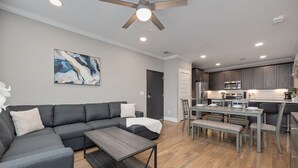 A modern living room with a gray sectional sofa, a wooden coffee table, and a dining area with a gray table and chairs.