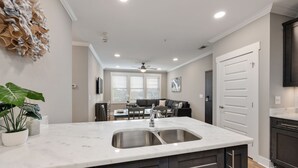 A modern kitchen with a double sink, dark cabinetry, and a dining area in the background.