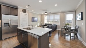 A modern kitchen with a built-in island, stainless steel appliances, and a dining area with a gray sofa and wooden table.