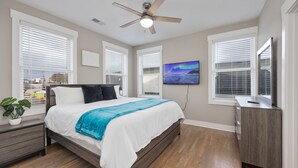 A bedroom with a bed, a ceiling fan, a TV, and a desk.