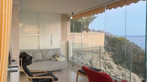 Un balcon avec un canapé et deux fauteuils, une vue sur la mer et un mur en pierre.
