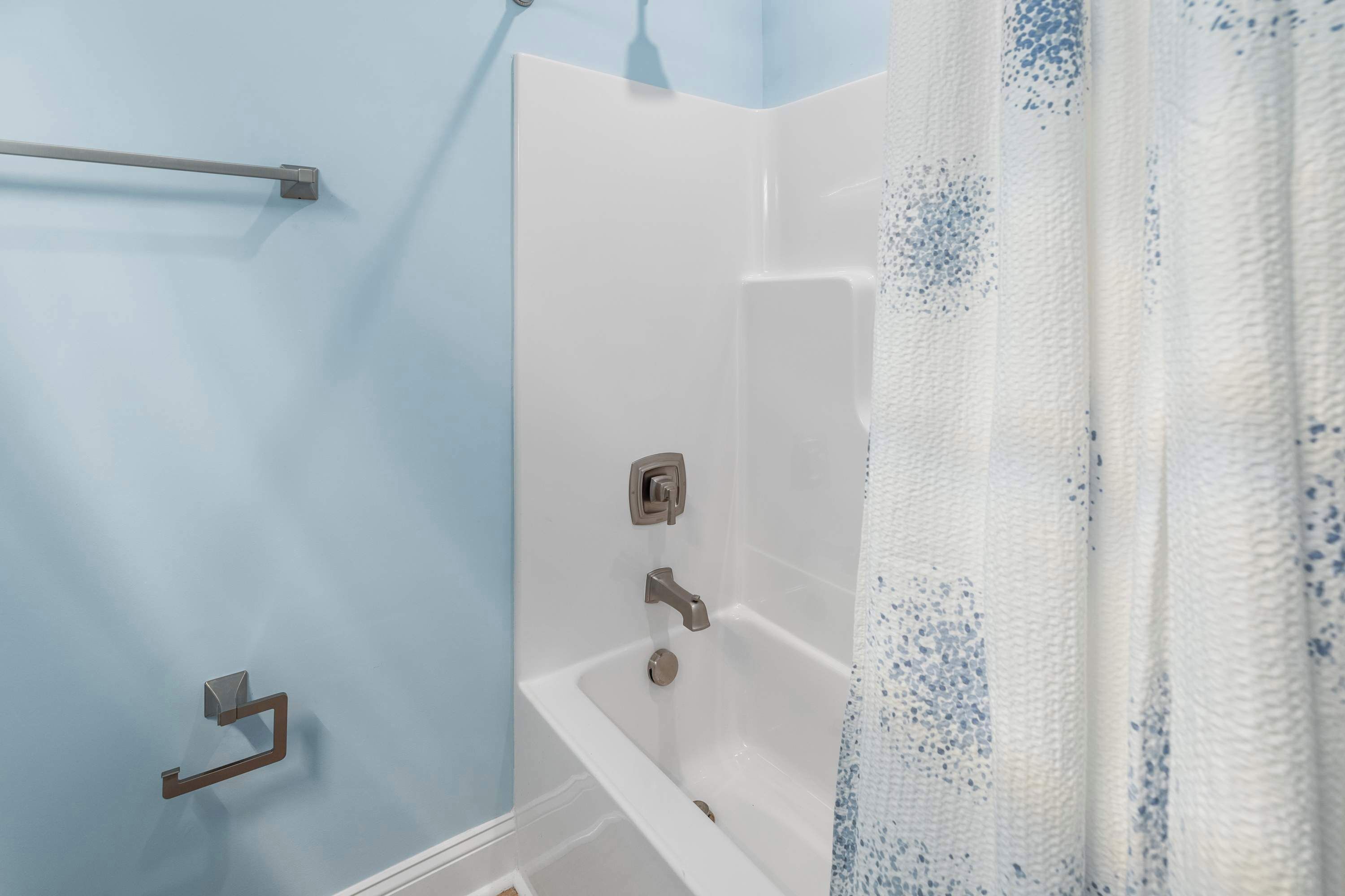Un baño con una bañera blanca, un perchero y una cortina de ducha.