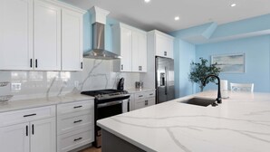 Ett modernt kök med vita skåp, en bänkskiva i marmor, rostfria vitvaror och en blå accentvägg.