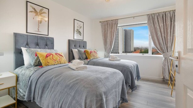 A double room with two beds, a window with curtains, and artwork on the walls. - Golf Road Apartment | Grampian Lettings (Aberdeen)