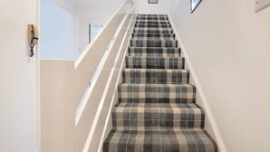 A staircase with a checkered carpet and white handrails. - Golf Road Apartment | Grampian Lettings (Aberdeen)