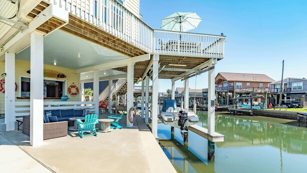 Une terrasse au bord de l’eau avec des sièges extérieurs, un espace couvert et un quai avec un bateau.