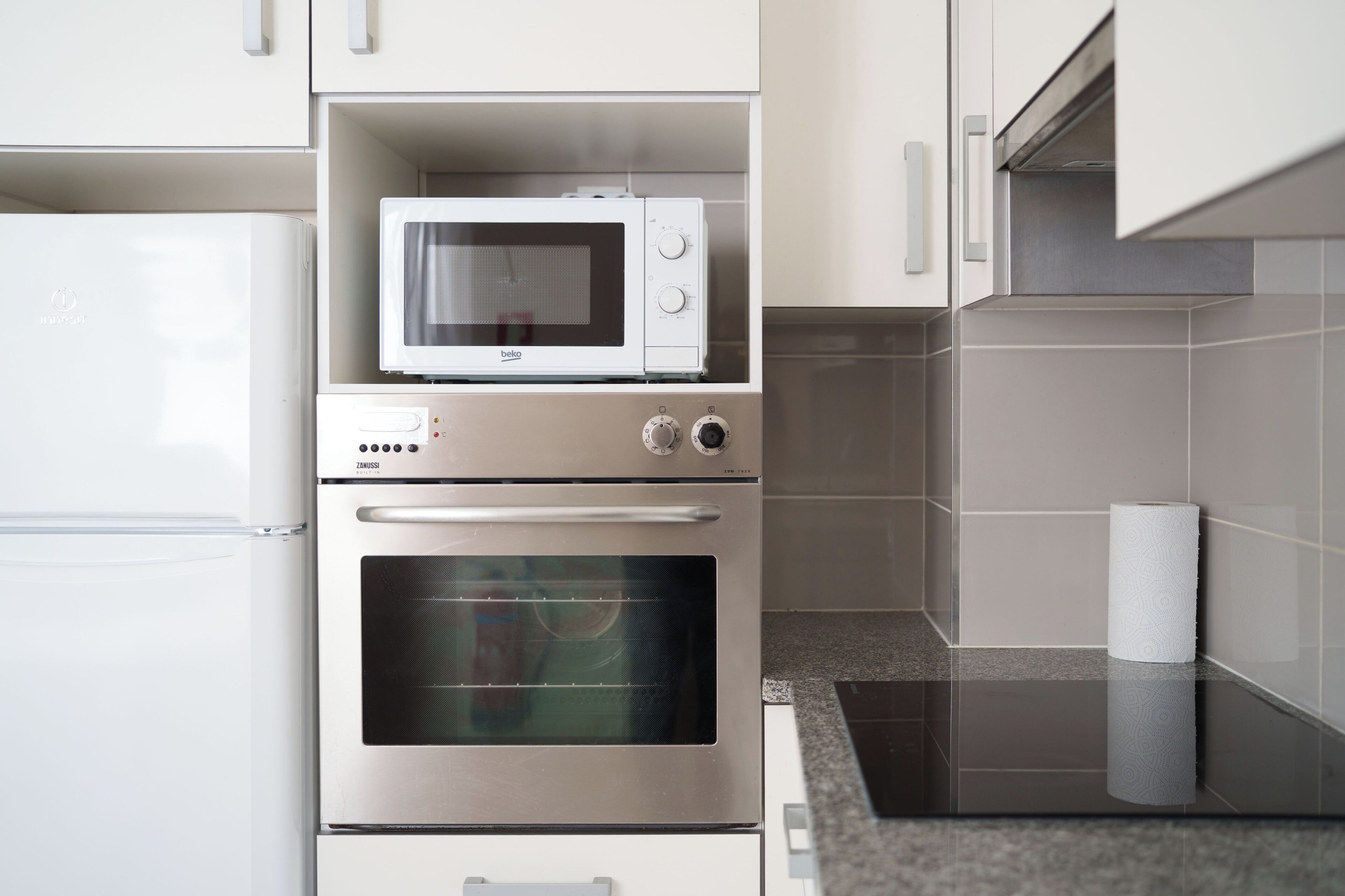 A kitchen with a built-in microwave, oven, and a refrigerator.